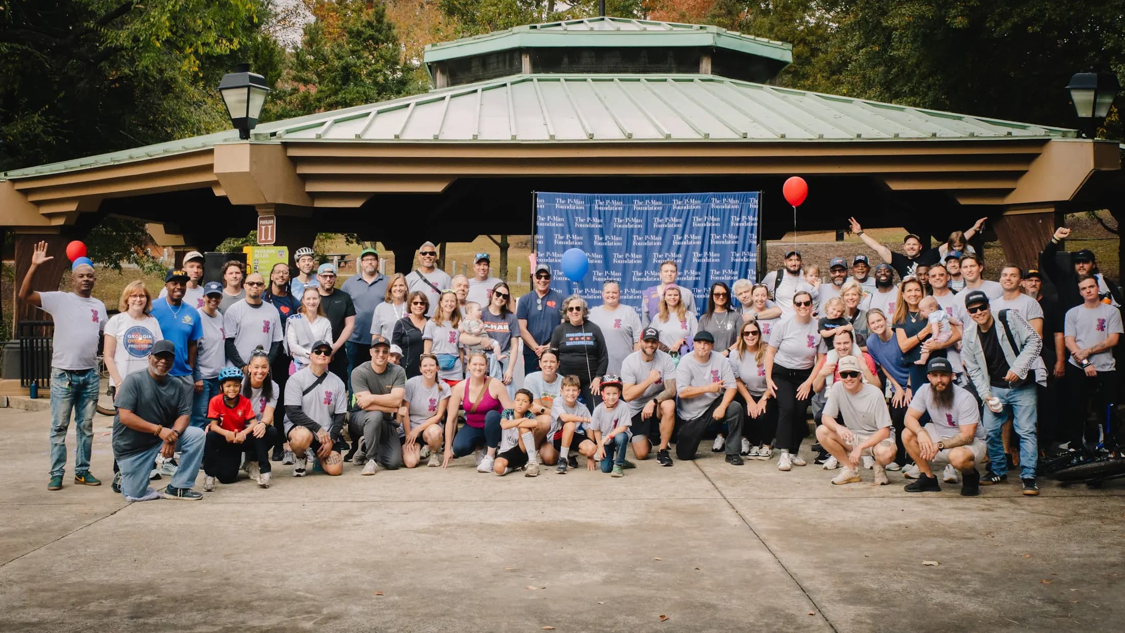 The 2025 Pedal for P-Man community gathers for a group photograph at the pavilion.
