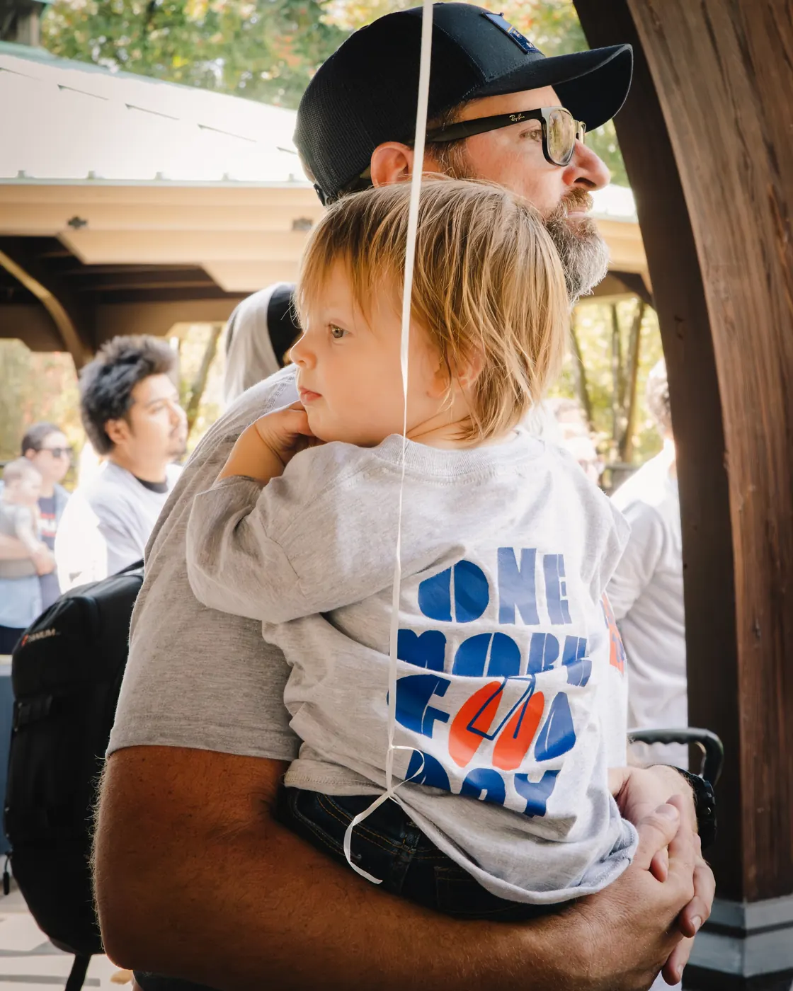 An adult holds a child wearing a One More Good Day shirt at the 2025 event.